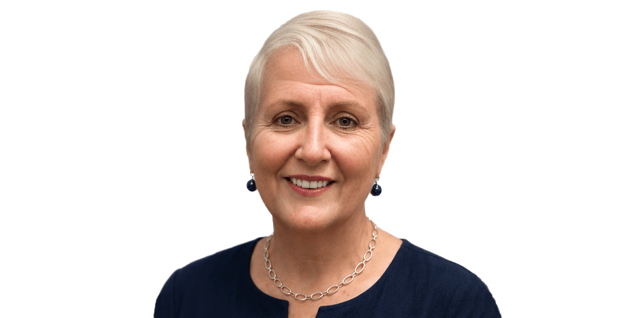 A photo of Joane Goulding, founder of the Goulding System, asmiling older woman with short gray hair, wearing a navy top, silver necklace, and dark blue earrings, against a plain light background.